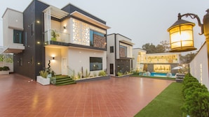 A modern two-story house with a pool, a well-lit entrance, and a balcony.