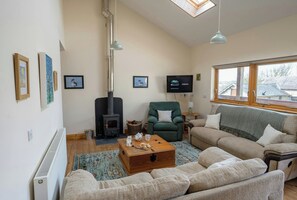 Un salon avec une cheminée, un fauteuil vert, un canapé beige et un téléviseur fixé au mur.