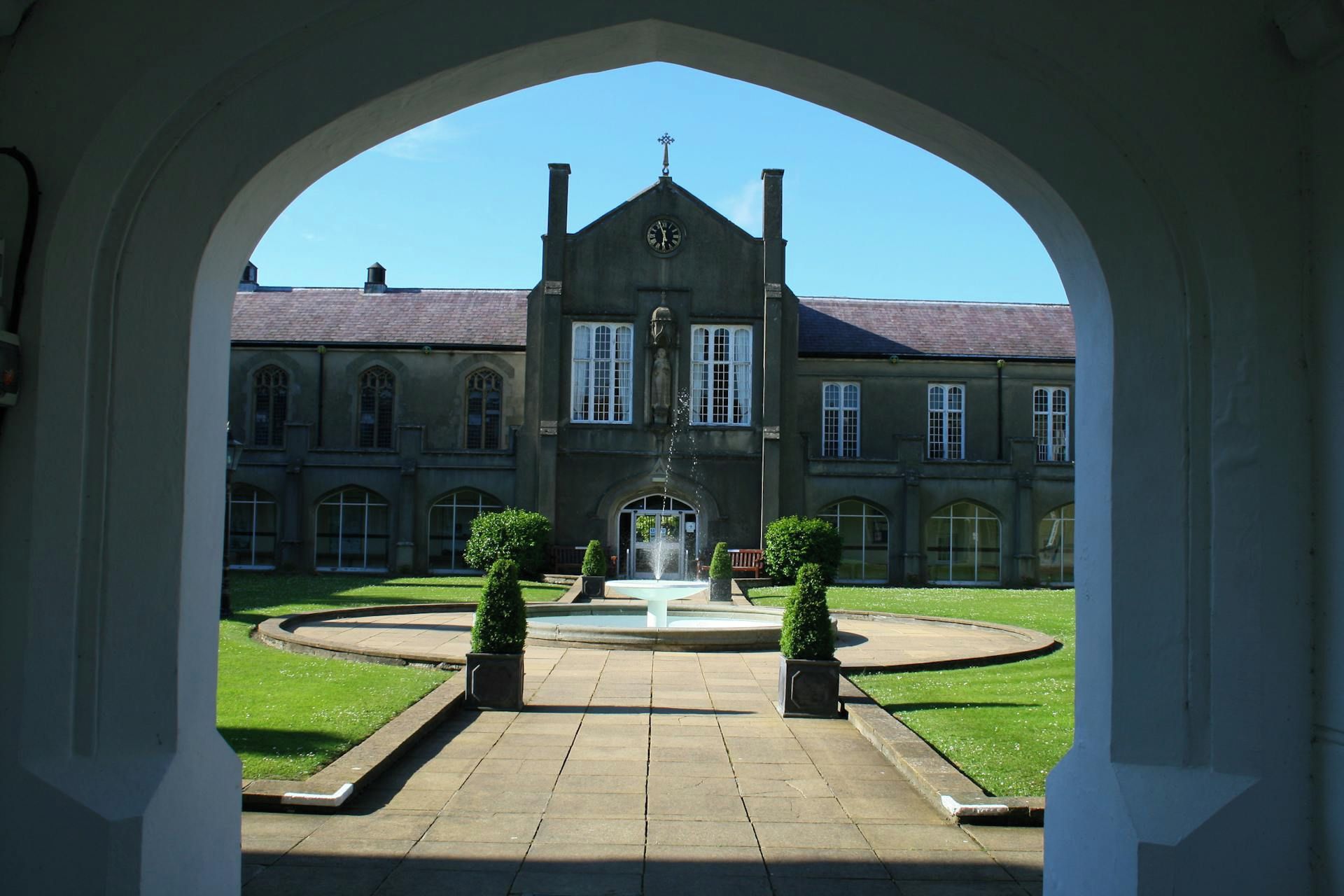A courtyard with a fountain, a building with arched windows, and a clear sky.