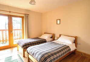 Una habitación con dos camas de madera, un ventanal corredero que da a un espacio exterior y un pequeño cuadro en la pared.
