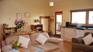 A cozy living room with a sofa, a dining table, and a kitchen area with a sink and cabinets. - Robin's Perch Eco Lodge Apartment, Lampeter (Lampeter)