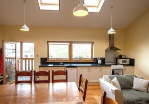 A spacious kitchen with a dining area, large windows, and a high ceiling. - Robin's Perch Eco Lodge Apartment, Lampeter (Lampeter)
