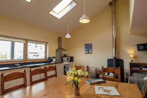 A kitchen with a dining table, chairs, a vase of flowers, a Scrabble game, and a television. - Robin's Perch Eco Lodge Apartment, Lampeter (Lampeter)