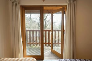 Wooden-framed glass doors opening onto a balcony with railing and trees beyond - Robin's Perch Eco Lodge Apartment, Lampeter (Lampeter)