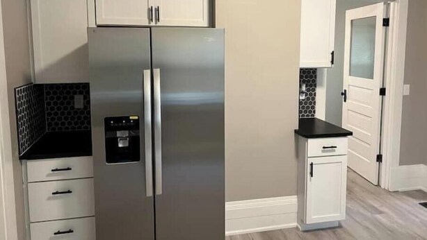 A kitchen with a stainless steel refrigerator, white cabinets, and a black countertop. - Just remodeled, for you! (Grand Rapids)