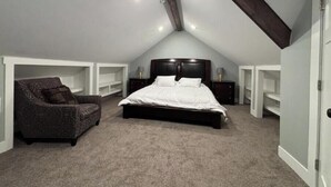 A bedroom with a sloped ceiling, a bed, a chair, and built-in shelving. - Just remodeled, for you! (Grand Rapids)