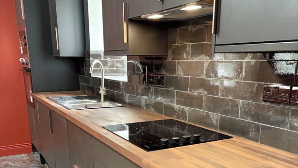 Eine moderne Küche mit Holztischplatte, Edelstahlspüle und dunklen Schränken.
