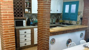 Une cuisine avec des arches en briques, des meubles blancs, un four à micro-ondes et une porte de couleur turquoise.