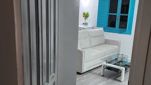 Un salon moderne avec un canapé blanc, une table basse en verre et une porte bleue.