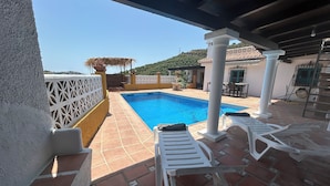 Une piscine avec un revêtement de sol en carrelage, des chaises longues blanches et une structure en forme de pergola.