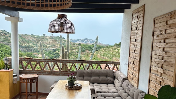 Une terrasse dotée d’un espace salon avec des coussins, d’une table agrémentée d’une plante en pot, et offrant une vue sur des cactus et des collines.