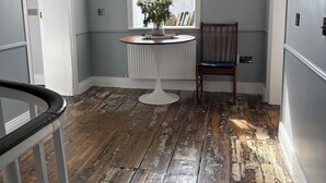 Une pièce dotée d’une grande fenêtre, d’une table ronde ornée d’un vase de fleurs, d’une chaise en bois et d’un plancher en bois.