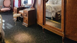 Une chambre à coucher de style traditionnel, avec un grand miroir, une armoire en bois, une coiffeuse avec un miroir, un lit avec une literie blanche et une chaise.