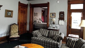 Une pièce comprenant un lit, un canapé à rayures, une chaise en bois et une table avec une lampe.