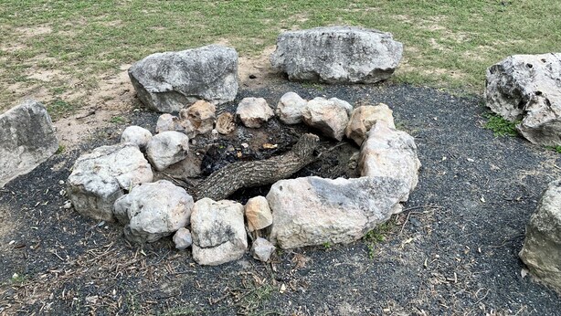A fire pit surrounded by large rocks in a grassy area.