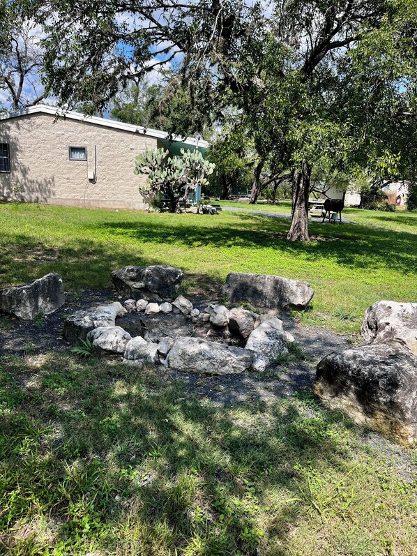 A stone building with a green roof, surrounded by a grassy area with large rocks and trees. - Charming 2-bedroom cabin right on the Frio River - Cabin #1 (Concan)