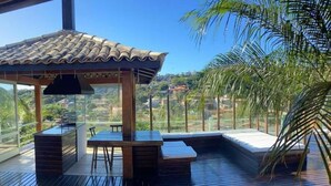 A wooden deck with a pergola, seating area, and a view of the surrounding landscape. - Casa 24 Búzios (Buzios)