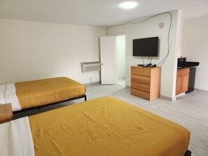 A room with two beds, a TV, a wooden dresser, and a microwave. - Economy Inn (Kingsland)