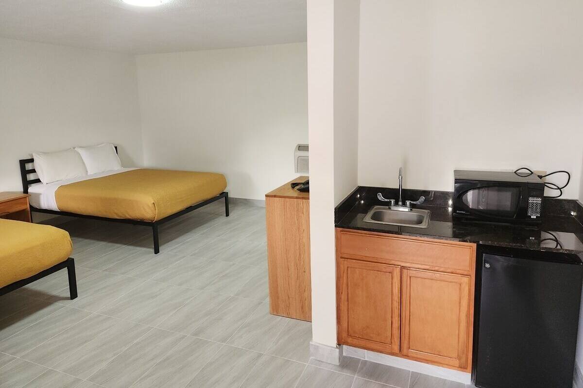 A compact room with two beds, a small kitchenette, and a white ceiling.