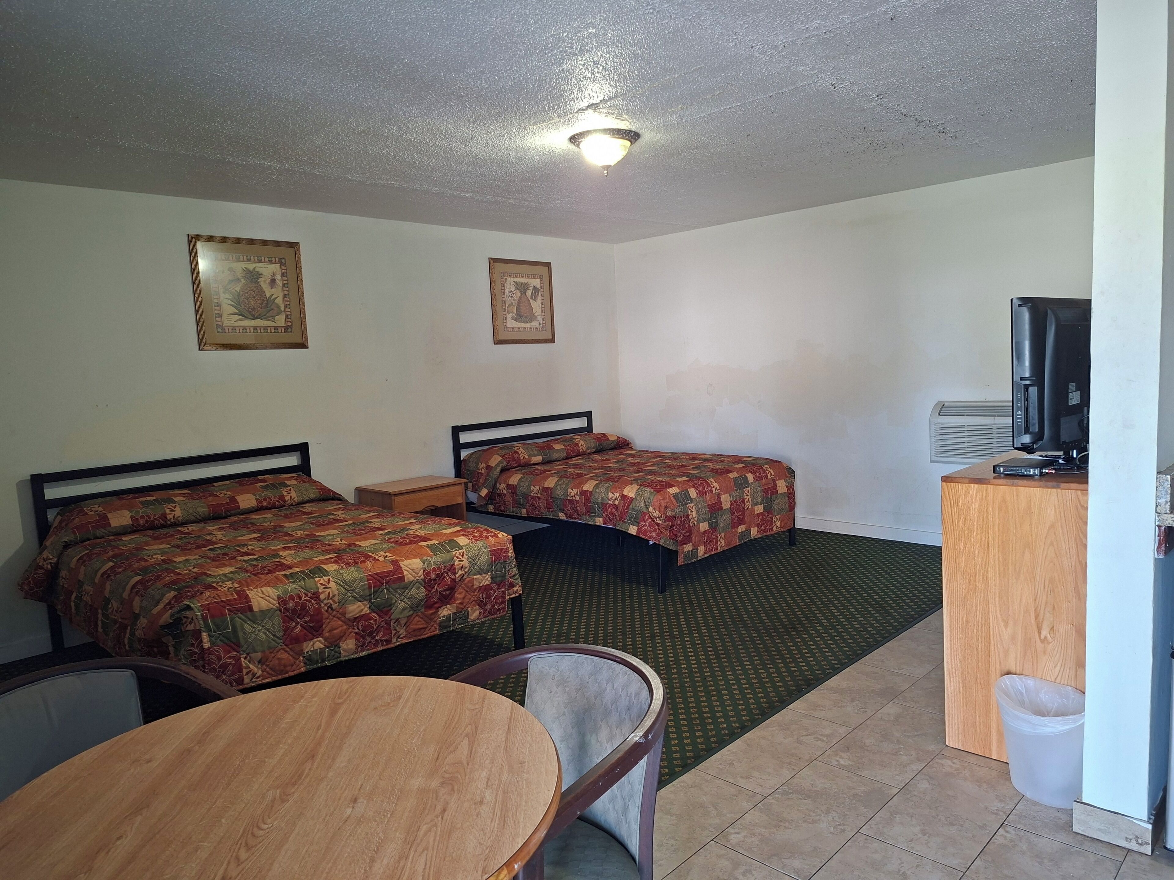 A hotel room with two beds, a desk with a computer, a television, and a small table.