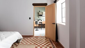 A bedroom with a bed, a checkered floor, a door leading to a kitchen with a window. - Casona 212 | Style, Connectivity & Parking (Unknown)