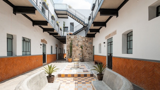 Un patio con piso de cuadros, plantas en macetas y una escalera que lleva a un nivel superior.