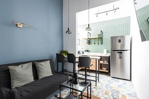 A compact living space with a sofa, two chairs, a coffee table, and a kitchen area with a refrigerator and a tiled backsplash.