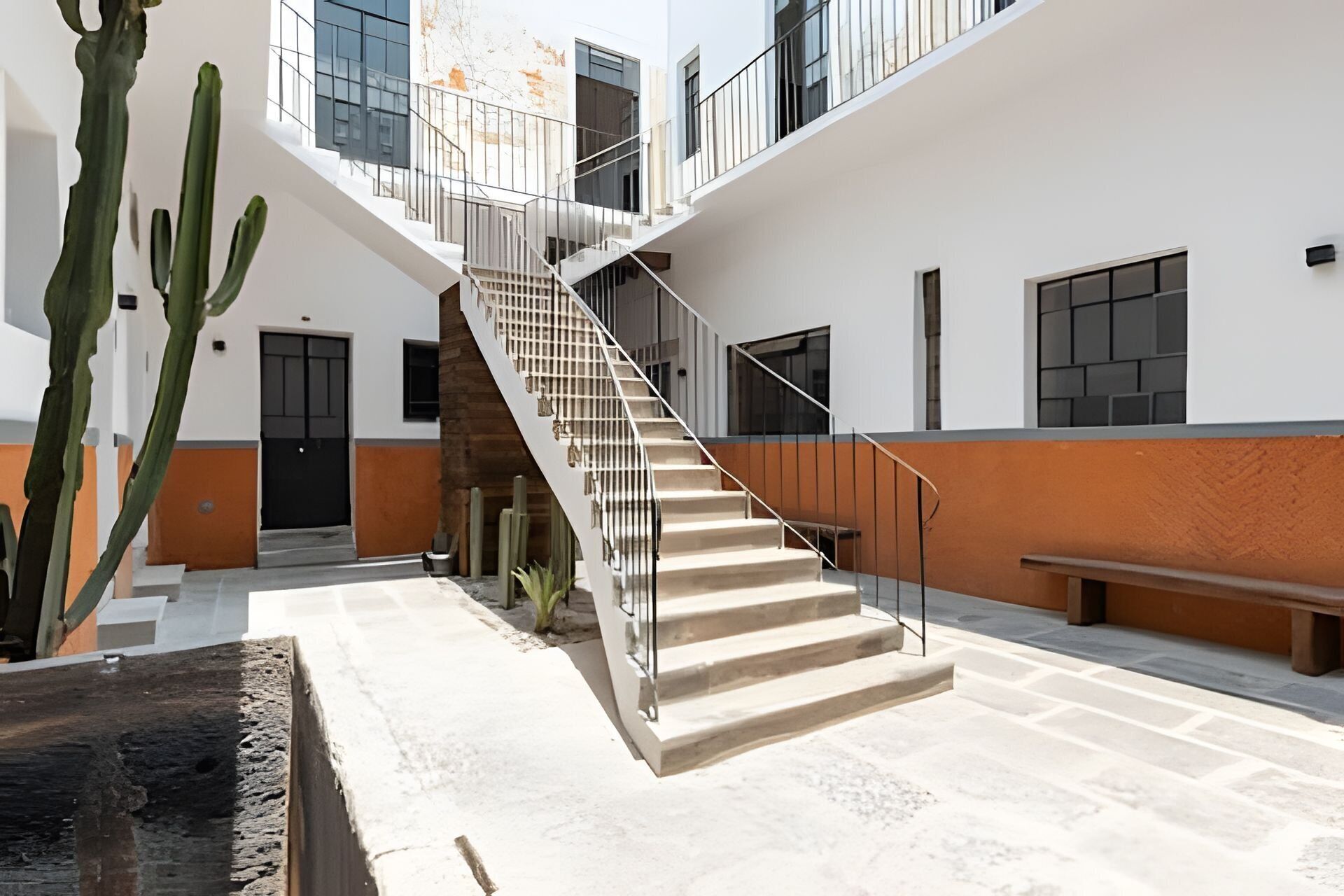 A modern building with a central staircase, a cactus, and a bench.