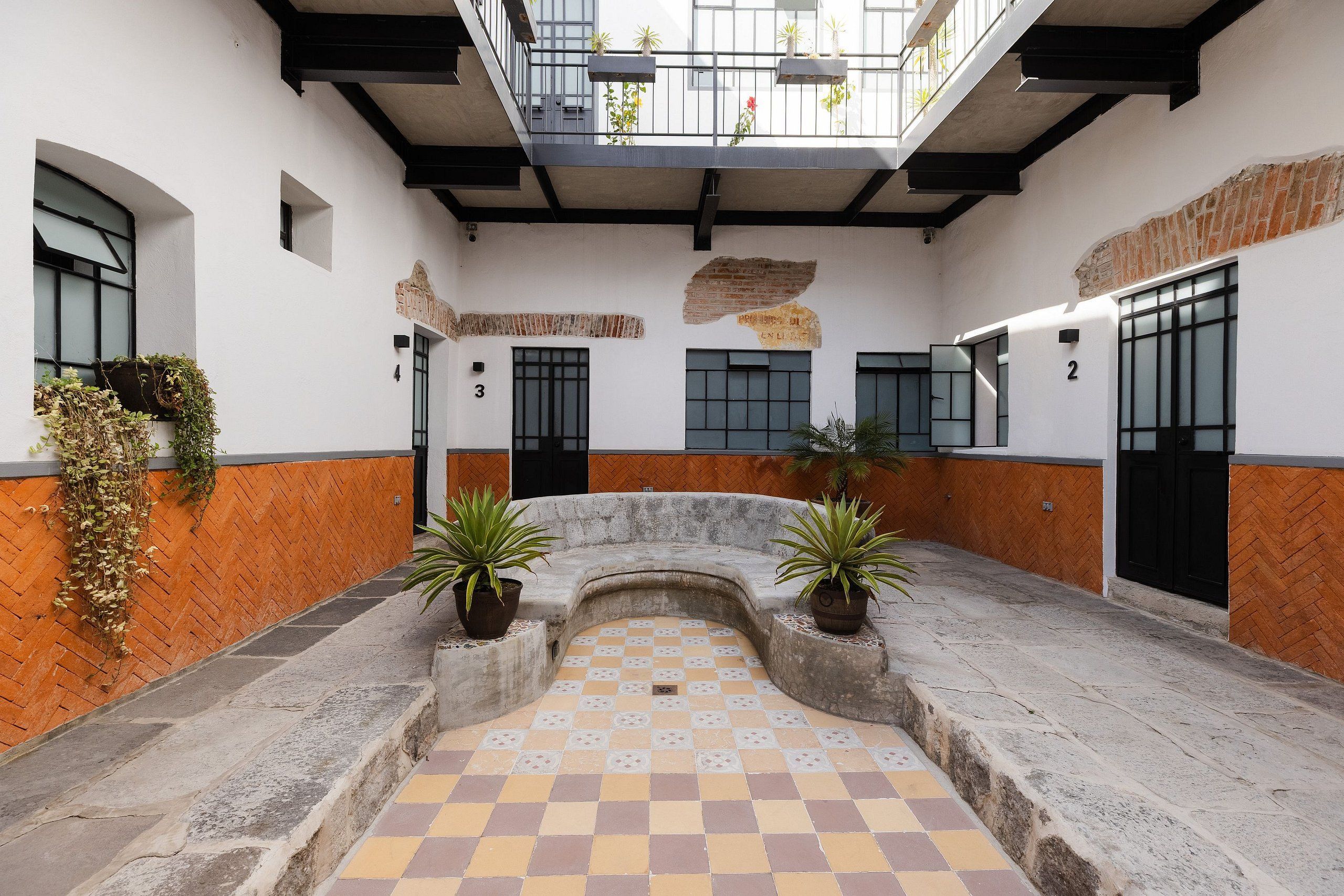 A courtyard with a checkered floor, potted plants, and a balcony with plants.