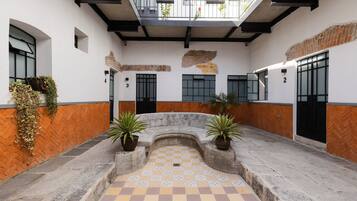 A courtyard with a checkered floor, potted plants, and a balcony with plants.