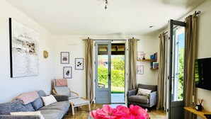 A living room with a sofa, a chair, a coffee table, and a TV. There is a door leading to a balcony. - Charming cottage with pool, air-Con, views & high speed WiFi (La Sauvetat-du-Dropt)