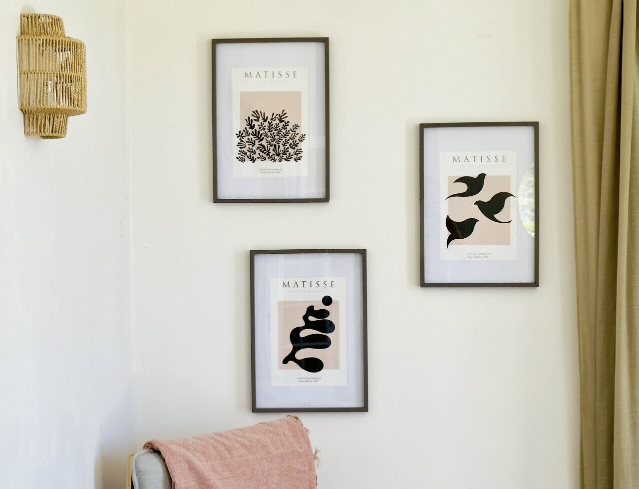 Tres obras de arte enmarcadas en una pared, un tapiz y una toalla rosa sobre una silla.