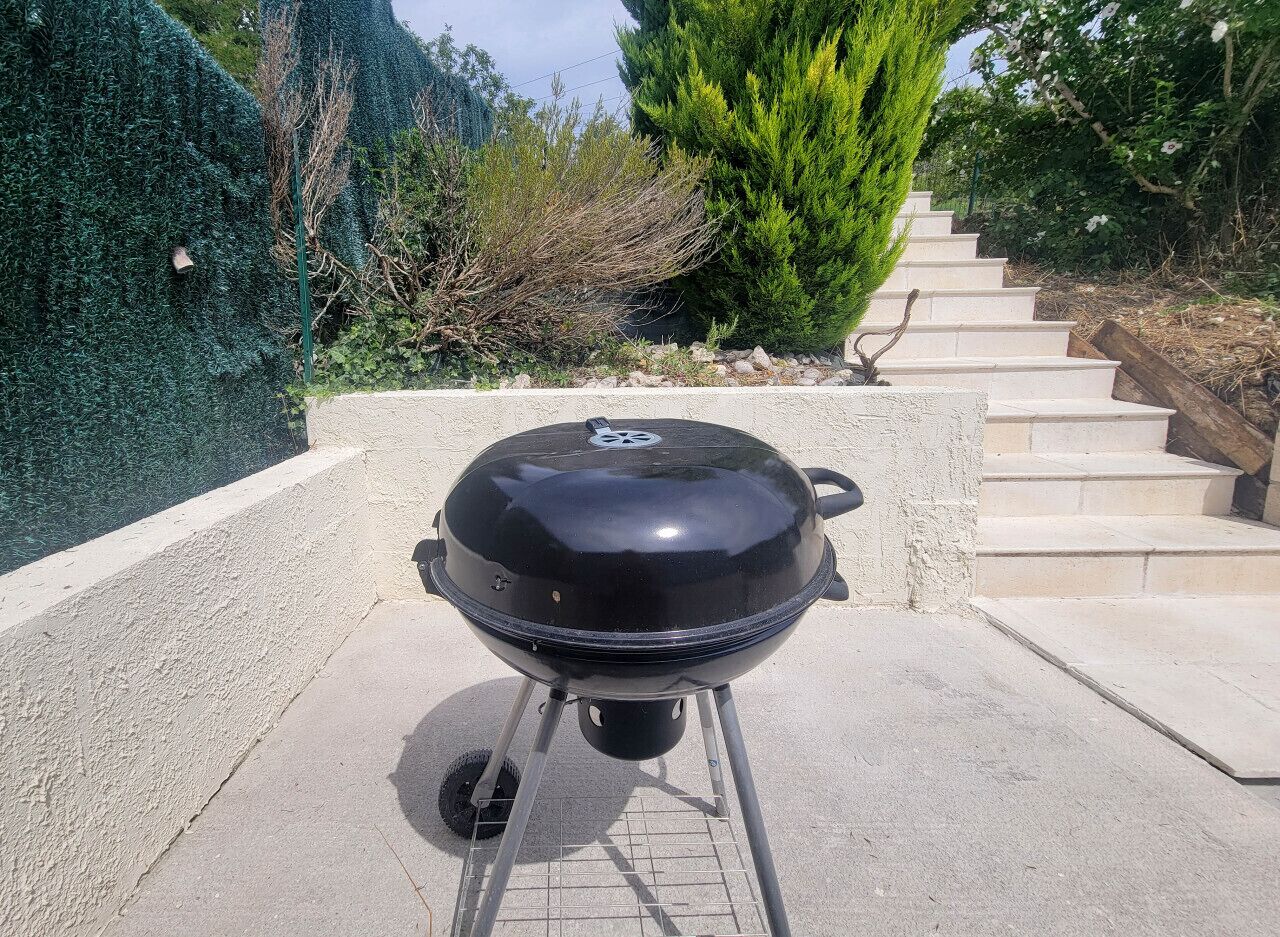 A black barbecue grill on a concrete patio with steps leading up to a wooden deck.