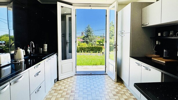A modern kitchen with a view of a garden through an open door. - Charming cottage with pool, air-Con, views & high speed WiFi (La Sauvetat-du-Dropt)