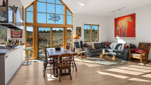 A spacious living area with a large dining table, a sofa, and a coffee table. There are large windows providing a view of the outdoors. - 25 Acre Artist Ranch, hot tub & tennis, near Aspen (Carbondale)