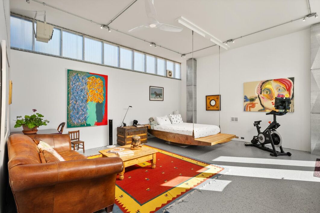 A modern living room with a sofa, a bed, an exercise bike, and artwork on the walls.