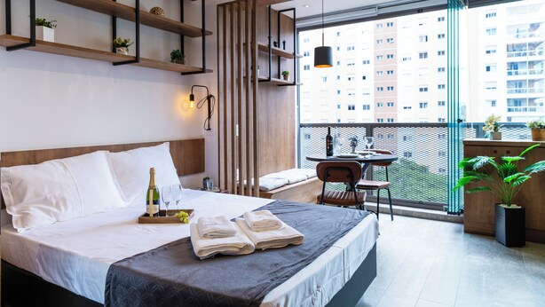 Una habitación de hotel moderna con una cama grande, mesita de noche y un balcón con vistas a la ciudad.