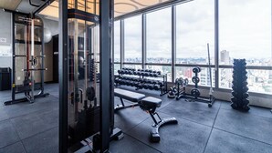 Un gimnasio con equipo de ejercicio variado, amplias ventanas y vistas a la ciudad.