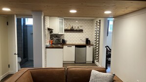 Un espacio habitable compacto con kitchenette, un sofá de cuero marrón y una zona de ducha.