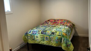 Una cama pequeña y bien hecha con un colcha de colores en una habitación con paredes blancas y una ventana.
