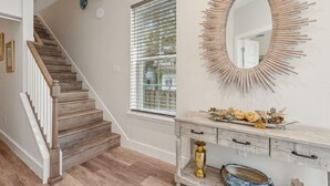 Una escalera con escalones de madera y barandillas blancas, una ventana con persianas, y un espejo con diseño de sol.