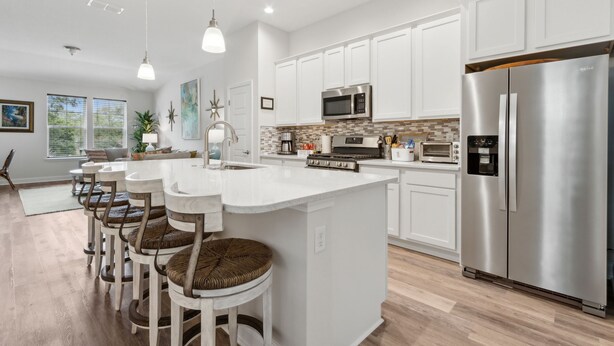 Una cocina moderna con armarios blancos, electrodomésticos de acero inoxidable y una isla central con taburetes de bar.