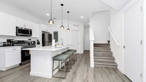 A modern kitchen with white cabinetry, a central island with bar stools, stainless steel appliances, and pendant lighting. - 6BR Chill Spot w/ Pool, Near Disney & Universal! (Davenport)