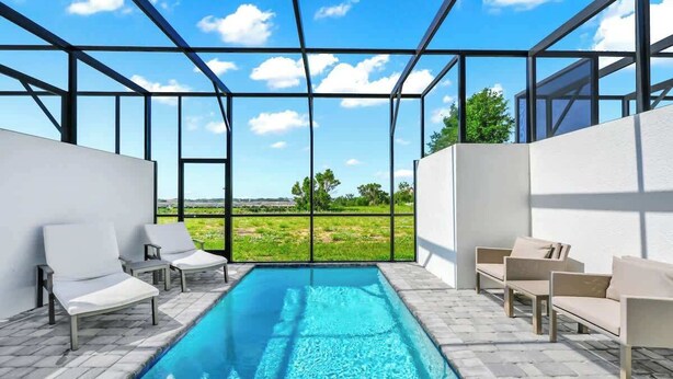 A pool area with clear blue water, surrounded by white lounge chairs and a glass enclosure with a view of a green landscape. - 6BR Chill Spot w/ Pool, Near Disney & Universal! (Davenport)