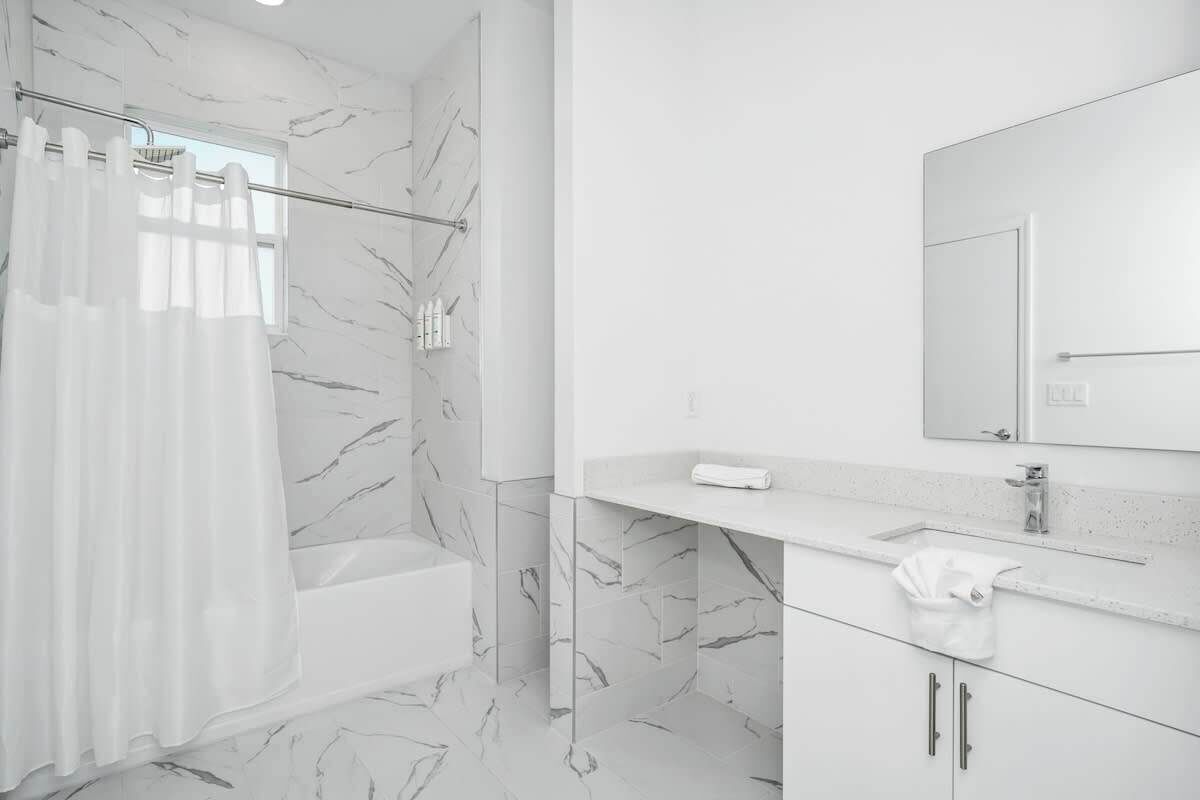 Un baño moderno con suelo de mármol, una bañera, una ducha con cortina, un lavabo con espejo y un perchero para toallas.