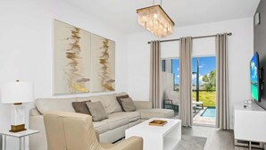 A modern living room with a beige sofa, a white coffee table, and a large abstract painting. - 6BR Chill Spot w/ Pool, Near Disney & Universal! (Davenport)