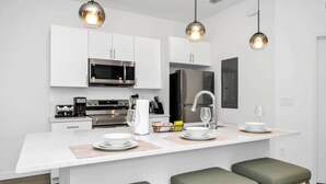 A modern kitchen with white cabinetry, stainless steel appliances, and a central island with bar stools. - 6BR Chill Spot w/ Pool, Near Disney & Universal! (Davenport)