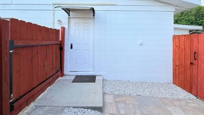 A white building with a red wooden fence, a door, and a small porch area.