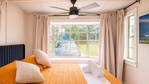 A bedroom with a bed, pillows, a ceiling fan, and a window with curtains.