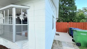 A house with a bay window, a red wooden fence, and two green trash bins.
